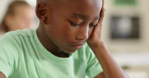 Concentrating African American boy studying at school desk, resting head on hand, thoughtful