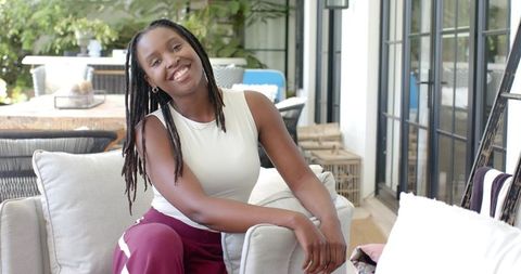 Smiling African Woman Relaxing on Sunroom Sofa Wearing White Top and Maroon Pants