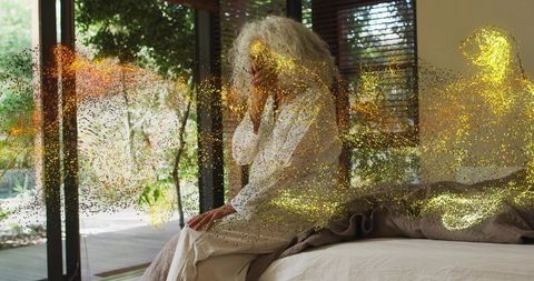 Silver-haired woman sitting on bed by glass doors with gold glitter overlay, serene