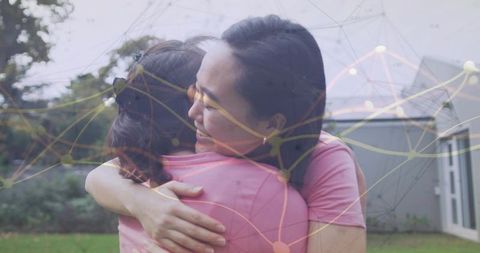 Two family members hugging in backyard wearing pink shirts with digital network overlay