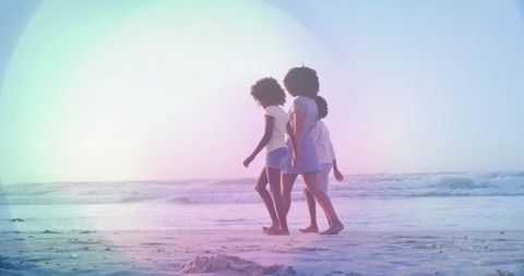 African american family walking along shoreline at low tide with pastel sunset lens flare