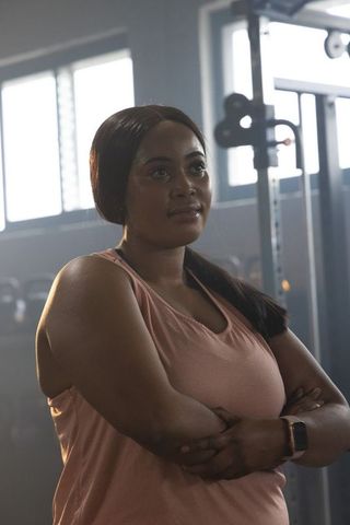 African american woman standing with arms crossed at gym wearing pink top and smartwatch
