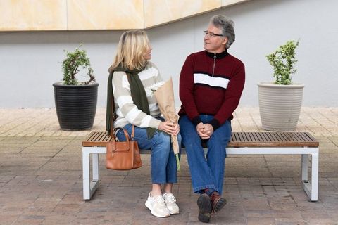 Senior couple sitting on bench sharing bouquet and conversation in urban courtyard plaza