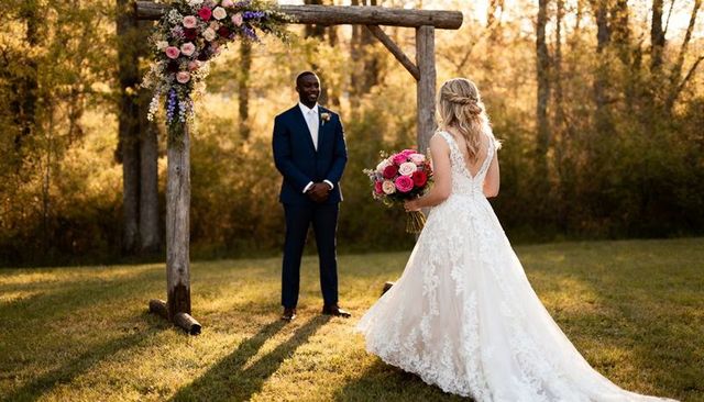Sunset rustic outdoor wedding couple exchanging vows beneath floral arbor