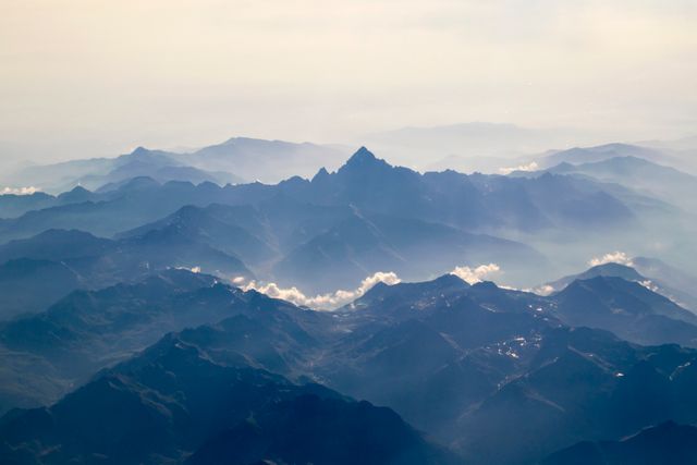 Breathtaking aerial view of a mountain range covered in mist at sunrise. Ideal for backgrounds, travel promotions, ecotourism, nature appreciation content, meditation apps, adventure blogs, and posters depicting serenity and natural beauty.
