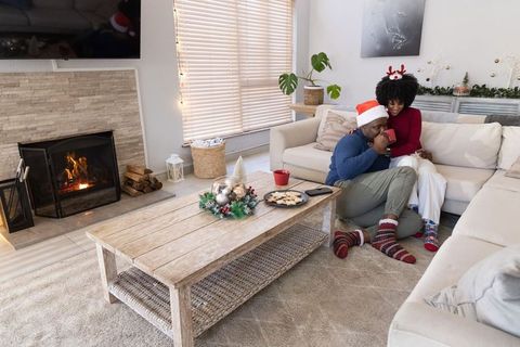 African american couple lounging by fireplace in santa hats enjoying cozy holiday evening