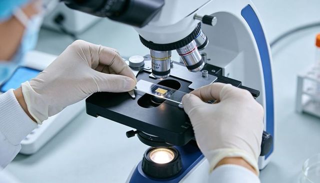Researcher placing slide under microscope for clinical laboratory analysis and precision