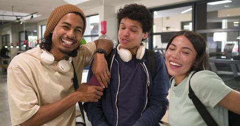 African american students laughing and chatting on campus with headphones and backpacks