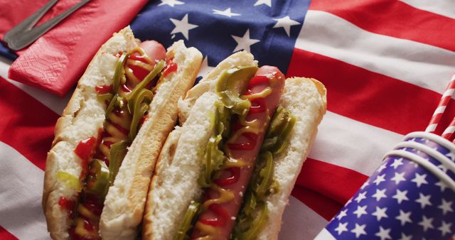 Tasty hot dogs topped with mustard, relish, and ketchup sit on a classic hot dog bun, placed on an American flag. Suitable for advertising summer barbecue events, Fourth of July celebrations, patriotic gatherings, American holidays, and food-related blogs or menus.