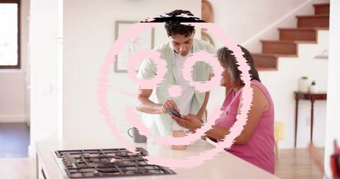 Young man helping older woman with smartphone at kitchen island, caring family moment