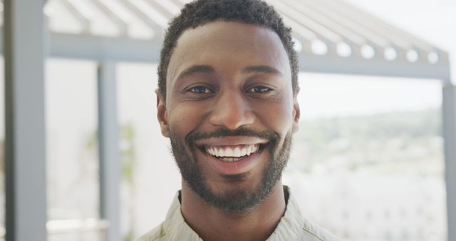 This image shows a smiling man enjoying the bright outdoor sunshine. Ideal for use in websites, advertisements, and campaigns promoting joy, confidence, and positive vibes.