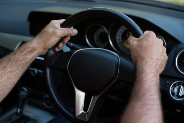 Hands gripping steering wheel while driving car. Ideal for illustrating concepts of road safety, transportation, and vehicle control. Useful for automotive advertisements, driving school materials, and travel-related content.
