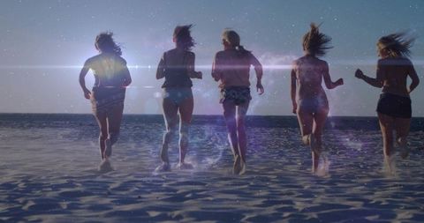 Five friends running on beach at sunset silhouettes splashing ocean horizon lens flare backlit