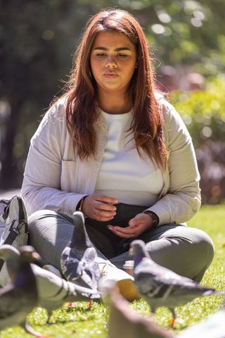 Woman sitting in park feeding pigeons on sunny day, candid outdoor portrait with bokeh
