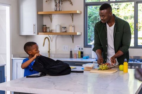 African american father preparing school lunch for son in modern kitchen morning routine