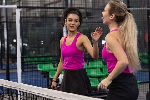 Padel partners celebrating point on indoor court wearing matching magenta tanks and black skirts