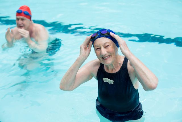 Senior man and woman enjoying swimming in a pool. They are wearing swim caps and goggles, engaging in a healthy and active lifestyle. This image can be used for promoting senior fitness programs, health and wellness campaigns, or aquatic exercise classes.
