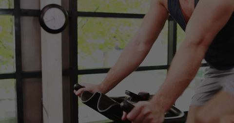 Pedaling man leaning and gripping handlebars on stationary bike with digital meter