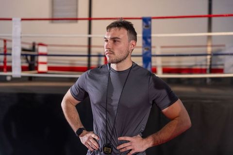 Boxing trainer standing hands on hips near ring showing focused determination