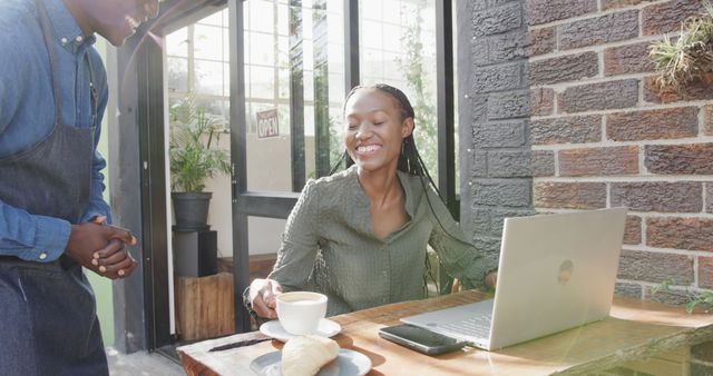 Smiling woman ordering coffee at cafe while working on laptop - Download Free Stock Images Pikwizard.com