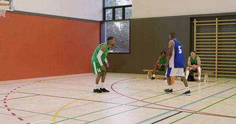 Black male basketball players practicing defensive drill and attack crossover in indoor gym