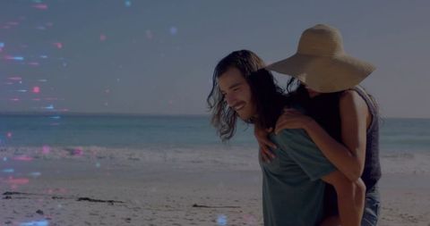 Couple enjoying piggyback walk on sunlit beach wearing straw hat by turquoise ocean