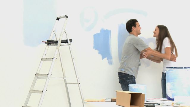 Couple embracing joyfully during home renovation, surrounded by painting supplies and a ladder. This scene emphasizes togetherness, creativity, and personal touch during home improvement projects. Useful for themes related to home design, marital relationships, teamwork, and DIY activities.