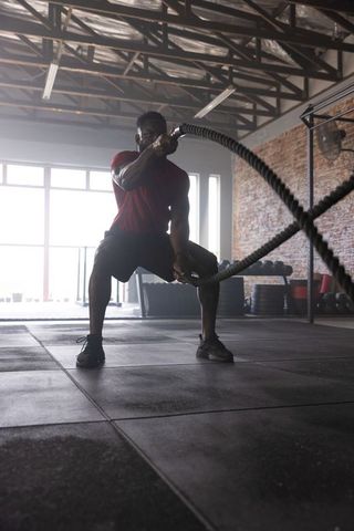 African american athlete training with battle ropes in backlit industrial gym