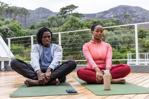 Practicing rooftop yoga and stretching by mountain view with african american friends