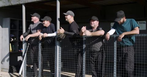 Sunlit baseball teammates leaning on dugout fence cheering and watching game