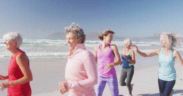 Group of senior women jog along a beach in the morning sunlight. They are dressed in brightly colored fitness clothing, enjoying the fresh sea air and each other’s company. Ideal for depicting active lifestyles, community health programs, and promoting outdoor physical activities among older adults.