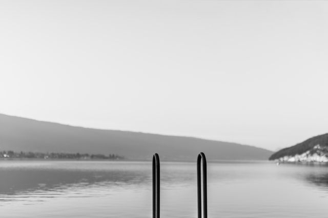 Peaceful and minimalistic black and white landscape with two vertical elements in foreground against tranquil lake and mountain background in day time. Ideal for creating a tranquil and serene atmosphere in any space. Perfect for themes of nature, solitude, and minimalism.