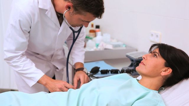 Doctor conducting a routine health check with a stethoscope, examining patient's arm for vital signs or blood pressure. Useful for illustrating medical consultations, healthcare services, doctor appointments, and diagnostic processes.