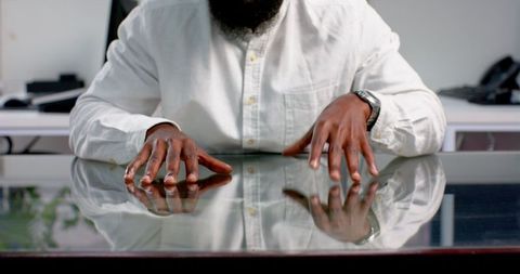 Businessman tapping fingers on glass desk in modern office