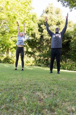 Woman and african american man stretching arms overhead on sunlit park lawn for fitness