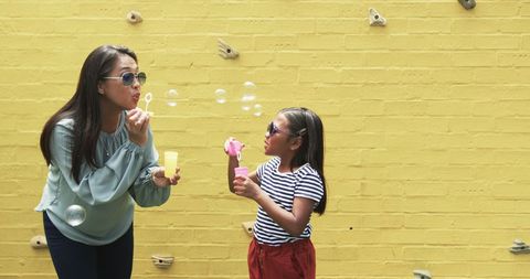 Mother and Daughter Blowing Bubbles Together Against Yellow Wall - Download Free Stock Images Pikwizard.com
