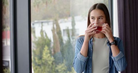 Woman Relaxing by Window Sipping Red Tea, Sunlight and Serene Environment