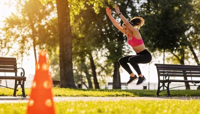 Woman performing plyometric jump in park during golden hour, outdoor fitness training