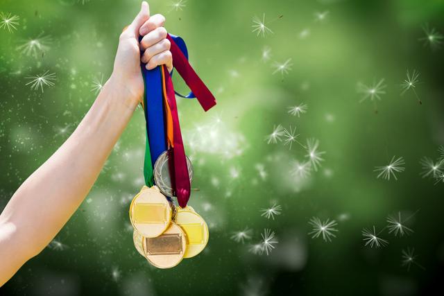 Hand holding multiple medals showing accomplishment and success with a green nature background. Suitable for themes related to achievement, competition, sportsmanship, and victory. Could be used for motivational or inspirational content in web and print materials, or as a representation of accolades and recognition in various presentations.