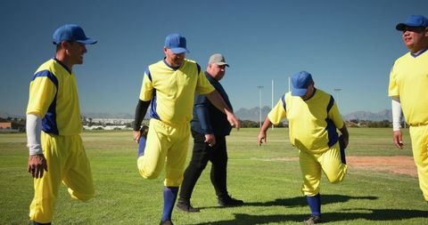 Amateur baseball team stretching on sunny field in yellow and blue uniforms