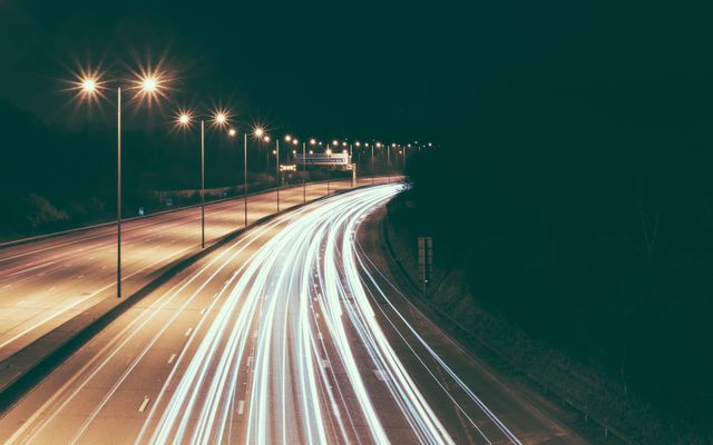 Long exposure photograph showing light trails from cars on a highway at night. Perfect for projects related to transportation, urban life, speed, or night photography. Can be used for websites, brochures, backgrounds, or travel-related advertising.