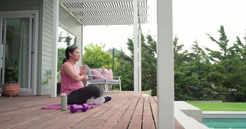 Mature woman meditating on deck by pool practicing mindfulness outdoor yoga and wellness
