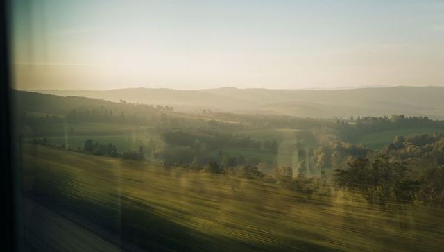 Golden-hour Countryside Passing by Window From Moving Train Over Rolling Farmland Panorama