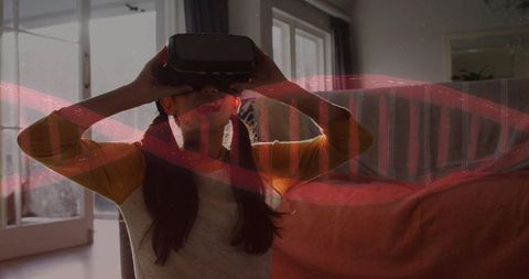 Chinese girl wearing vr headset exploring virtual world at home on sofa with ribbon light