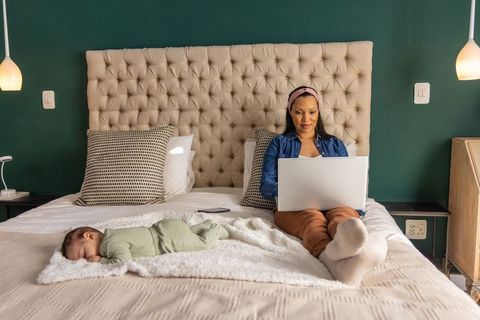 Remote working mom on bed with sleeping infant, laptop balancing parenting and career
