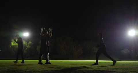 Four players practicing night football under bright floodlights on outdoor grass field
