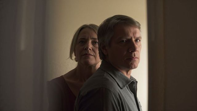 Moody intimate middle-aged couple standing in narrow hallway with warm side lighting