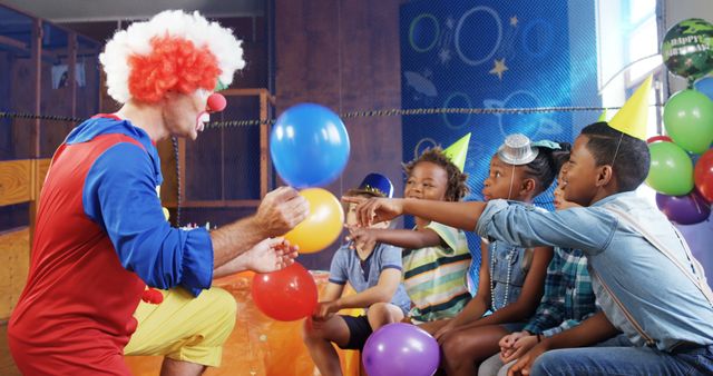 A clown entertains a group of African American children at a festive birthday party, with copy space. Balloons and colorful decorations enhance the joyful atmosphere as the kids engage with the performer.