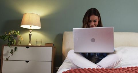 Woman working comfortably on laptop in cozy bedroom environment