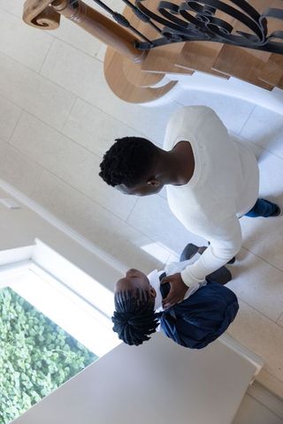 Parent guiding child with backpack through bright foyer, hand on shoulder, departure